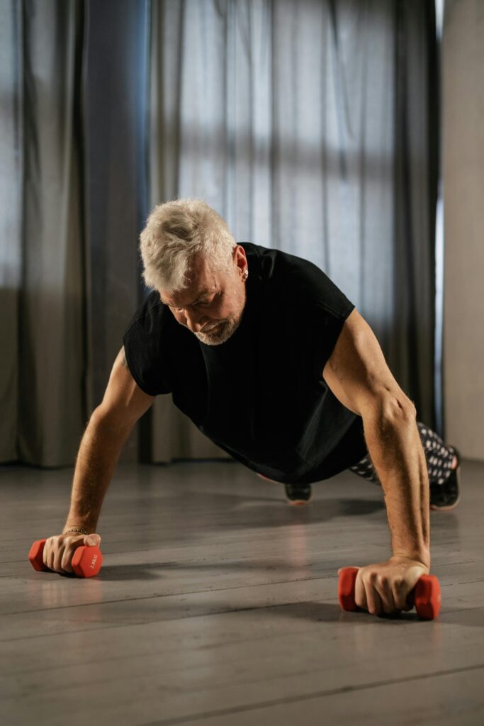Senior em treino de força em academia com luz natural e supervisão
