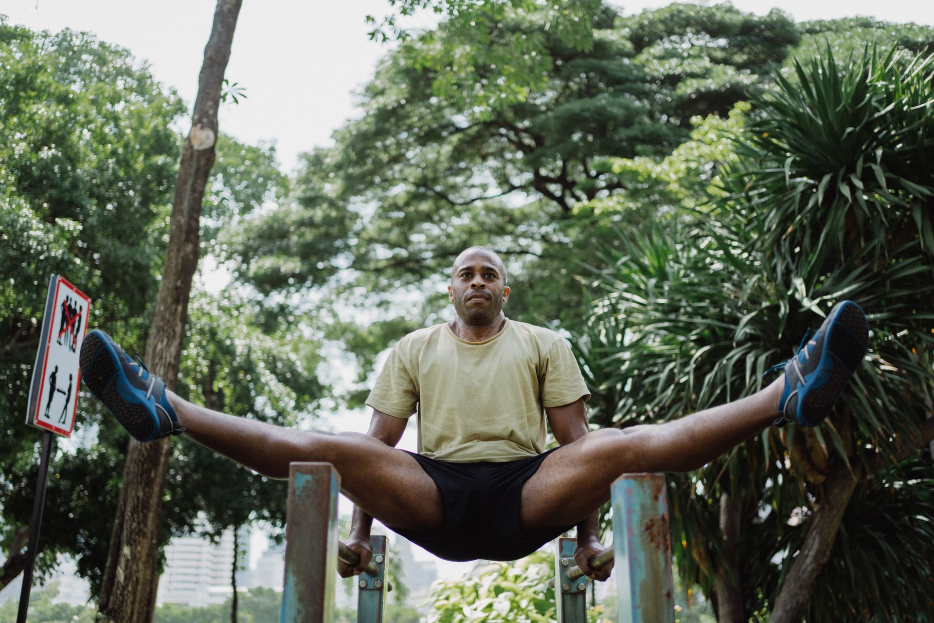 Homem usando barras paralelas de aparelho de ginástica pública em parque, equipamento ao ar livre em uso