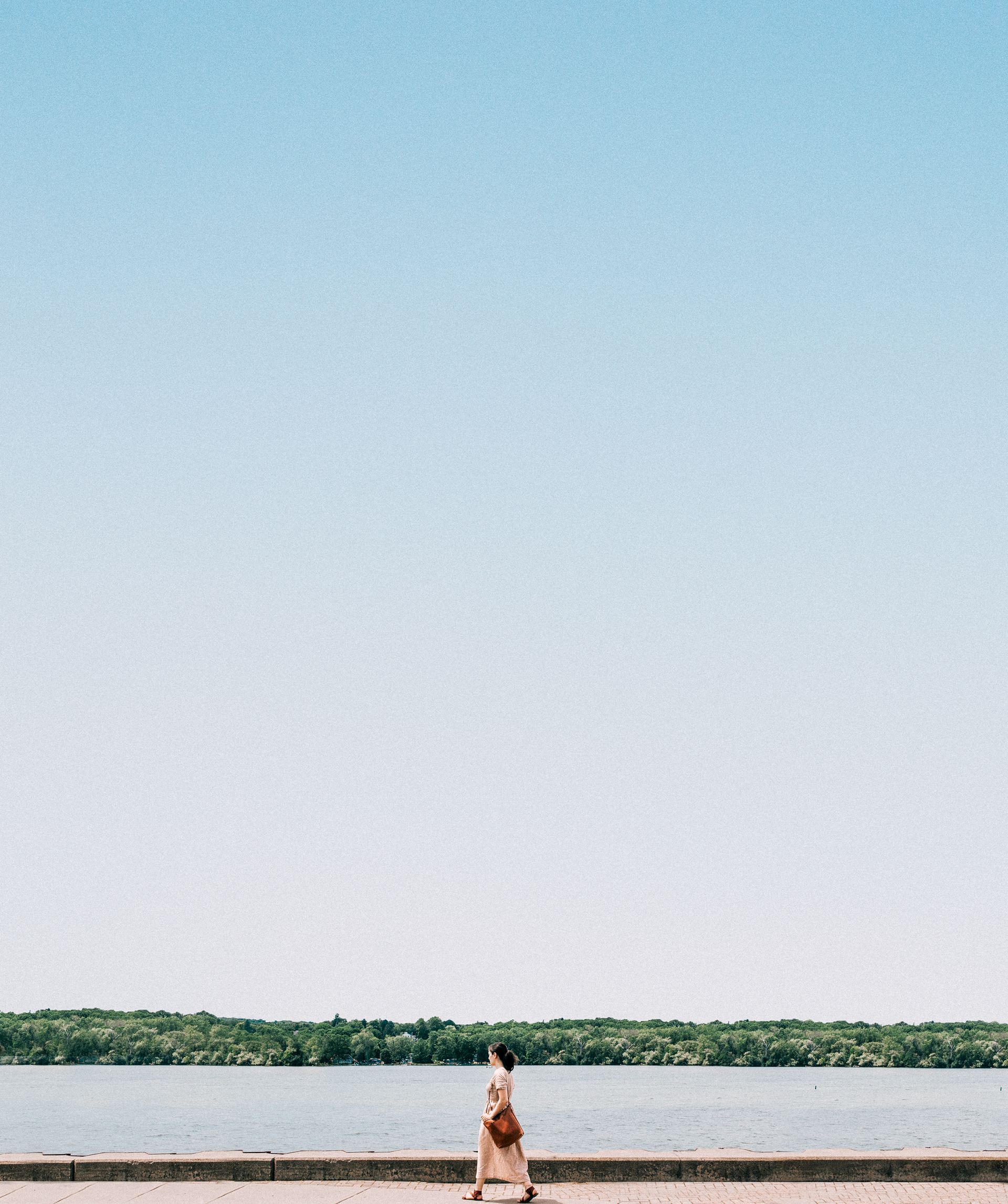 Mulher caminhando na orla de um lago em dia claro, caminhada como primeiro passo de quem voltou a treinar